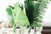 a cluster wedding centerpiece of vases and bottles, tropical leaves, greenery and fern is a lovely idea for a tropical wedding
