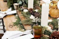 a cozy rustic Christmas table with evergreens, berries, pinecones, pillar candles and white hydrangeas
