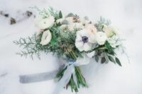 a delicate and subtle wedding bouquet of white ranunculus and anemones, evergreens and foliage and grey ribbon