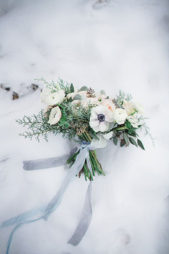 a delicate and subtle wedding bouquet of white ranunculus and anemones, evergreens and foliage and grey ribbon