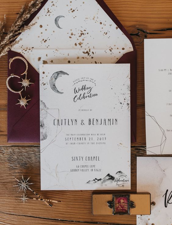 a gorgeous celestial wedding invitation suite with a burgundy envelope, white invites and watercolors, gold foil is wow