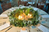 a greenery table centerpiece with eucalyptus, ferns and candles is a unique wreath-like piece