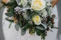 a lovely snowy winter wedding bouquet of white blooms, pale greenery, evergreens, pinecones, baby’s breath and twigs is amazing
