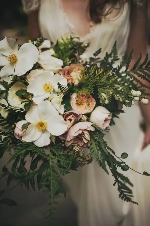 a pastel woodland wedding bouquet with greenery, ferns, white and pink blooms and berries looks very relaxed and spring like