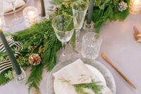 a pretty evergreen winter table runner with snowy and bleached pinecones, ribbon, tall and thin green candles