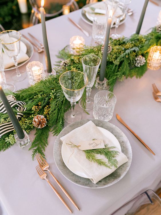 a pretty evergreen winter table runner with snowy and bleached pinecones, ribbon, tall and thin green candles