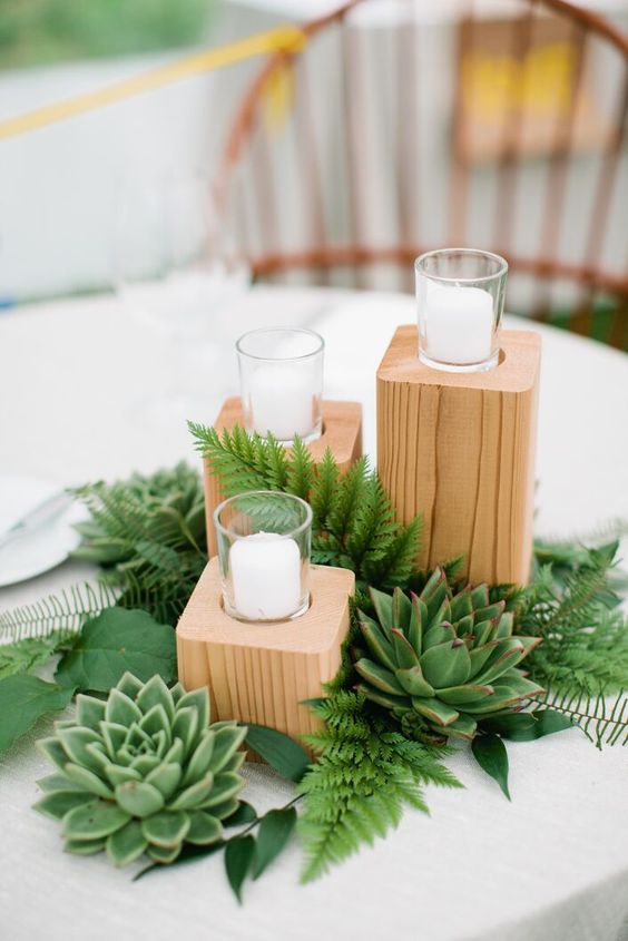 a pretty rustic wedding centerpiece of fern, leaves, succulents, wooden slabs holding candles is a lovely idea
