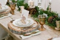 a rustic Christmas wedding tablescape with an evergreen and pinecone runner, various candles and wood slice placemats