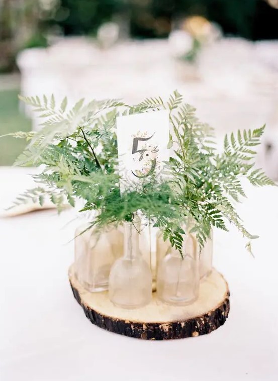 a rustic centerpiece with a wood slice, some ferns in bottles and a table number is very easy to DIY