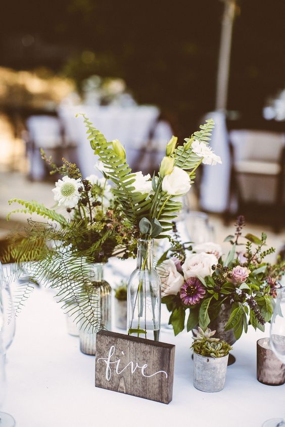 a rustic cluster wedding centerpiece of white, mauve and pink blooms, fern and greenery and some succulents