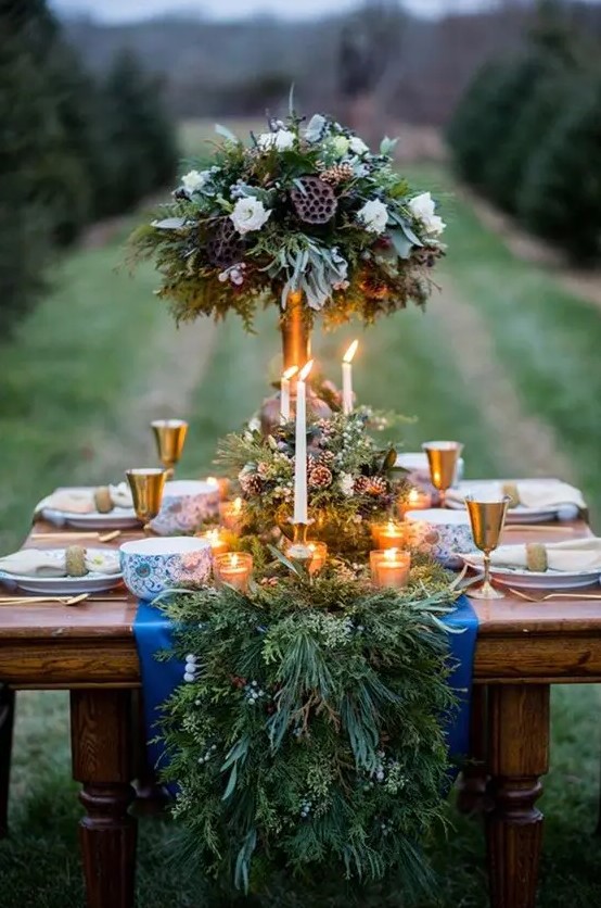 a rustic evergreen table runner with berries and pinecones and lots of candles bring winter spirit