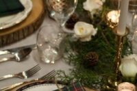 a rustic winter wedding table setting with plaid napkins, cinnamon, evergreens, white blooms and pinecones