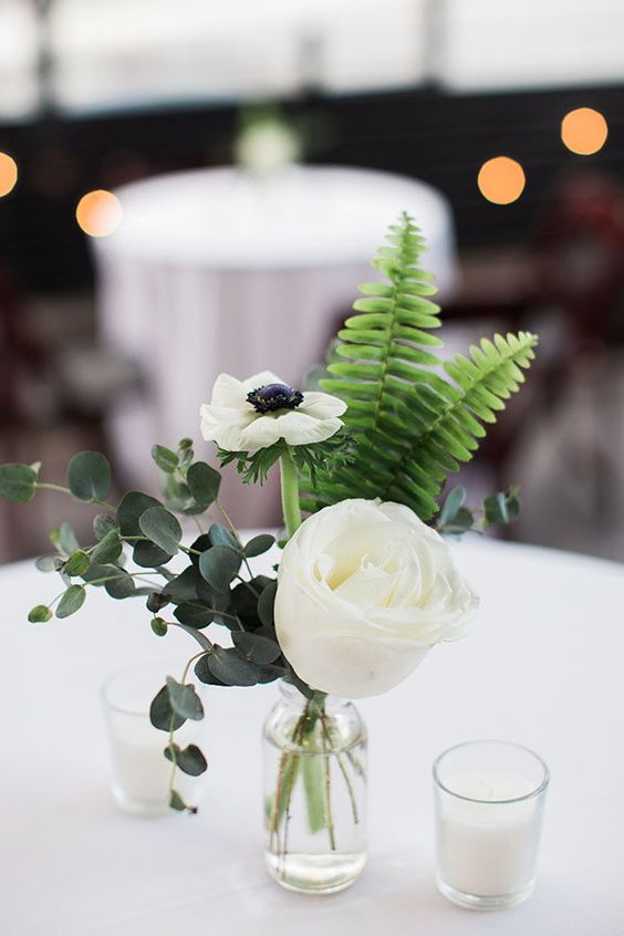 a simple and elegant wedding centerpiece of a white rose and anemone, eucalyptus and fern, a couple of candles is a cool idea