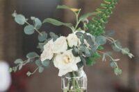 a simple and stylish wedding centerpiece with white garden roses, fern and eucalyptus and a couple of candles on each side
