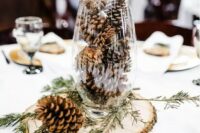 a simple rustic winter wedding centerpiece of a wood slice, a tall glass with pinecones and evergreens is very easy and fast to DIY