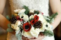 a small and chic Christmas wedding bouquet of evergreens, white roses and ranunculus, white anemones, berries, pinecones