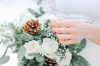 a small and lovely wedding bouquet of white roses and baby’s breath, evergreens and eucalyptus, pinecones is a cool idea for winter