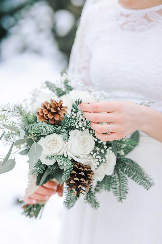 a small and lovely wedding bouquet of white roses and baby's breath, evergreens and eucalyptus, pinecones is a cool idea for winter