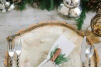 a stylish rustic place setting with a wood slice, cinnamon and evergreens plus an evergreen runner with pinecones