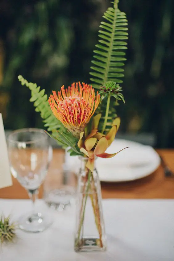 a tropical wedding centerpiece of a couple of tropical blooms and fern is a lovely and cool idea for a modern wedding