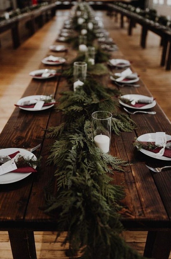 a very simple rustic tablescape with an uncovered table, a fern runner and evergreens, burgundy napkins