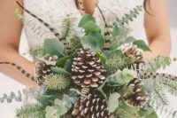 a winter wedding bouquet made of greenery, evergreens, feathers and snowy pinecones is a cool idea for a woodland bride