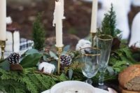 a winter wedding centerpiece of evergreens, ferns, snowy pinecones, cotton and candles in candle holders for a Christmassy table setting