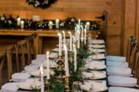 a winter wedding tablescape with gold touches, emerald napkins and a runner of evergreens, candleholders and a table number
