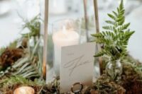 a woodland wedding centerpiece with moss, ferns, candleholders and a candle lantern plus a table number is very chic and beautiful