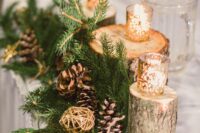 a woodland winter wedding centerpiece of evergreens, pinecones, gilded yarn balls and candleholders on tree stumps