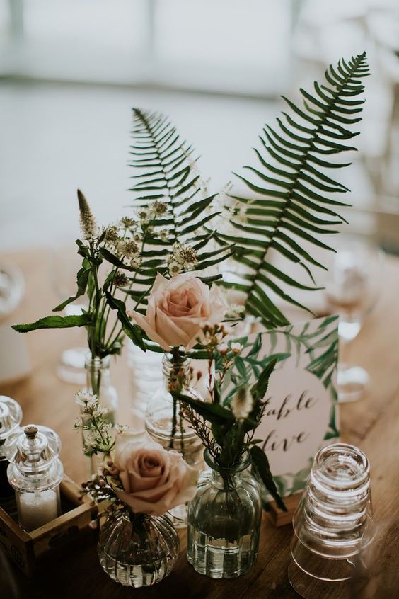 an elegant cluster wedding centerpiece of white blooms and blush roses, fern and a fern print table namde plus some candles