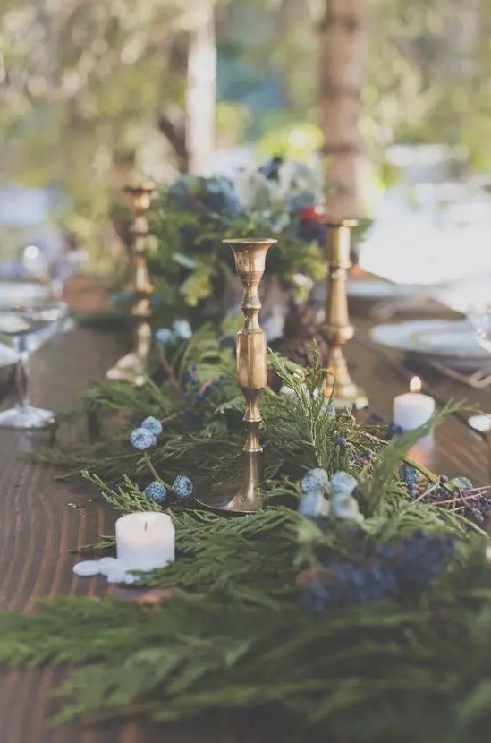an evergreen table runner with blue flowers and blueberries, dotted with candles, for a natural feel