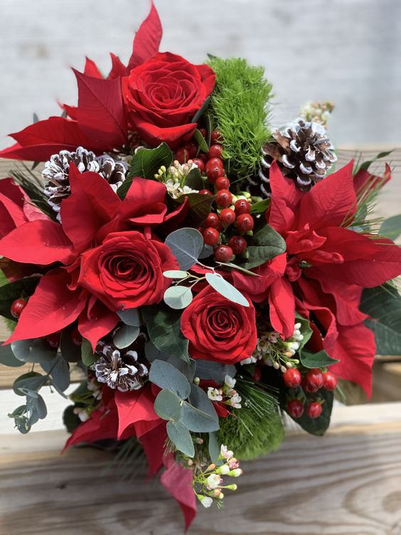 a winter wedding bouquet with red roses and poinsettias, snowy pinecones, berries and greenery is a bold and cool idea