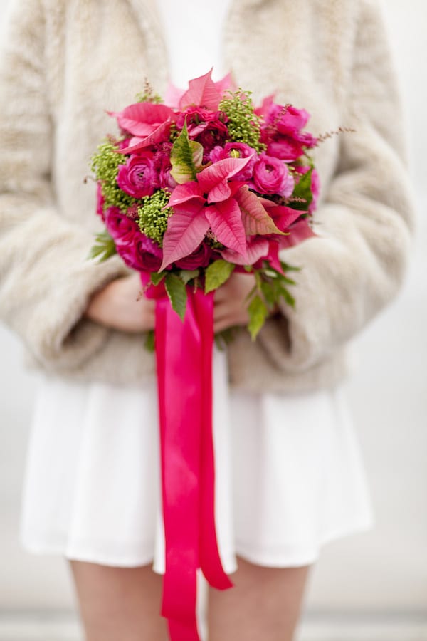 a bold wedding bouquet with hot pink ranunculus and poinsettias, greenery and green berries plus long pink ribbons