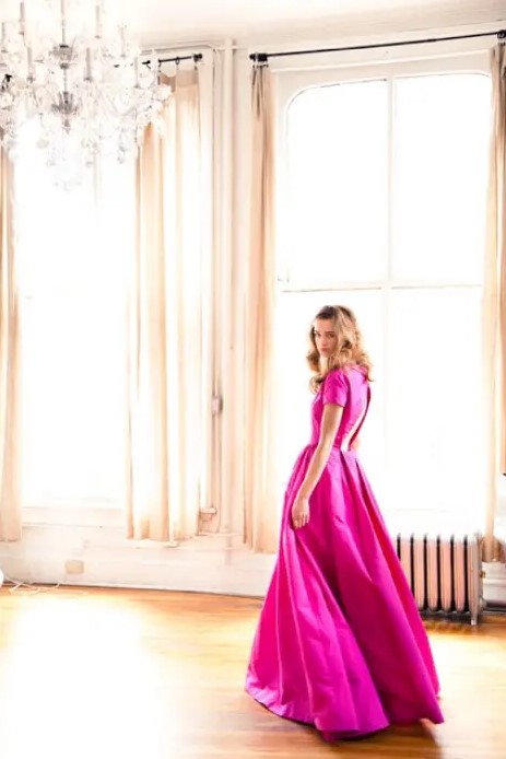 a bride rocking an unusual magenta A-line wedding dress with a cutout back, short sleeves and a pleated full skirt looks bold and stylish