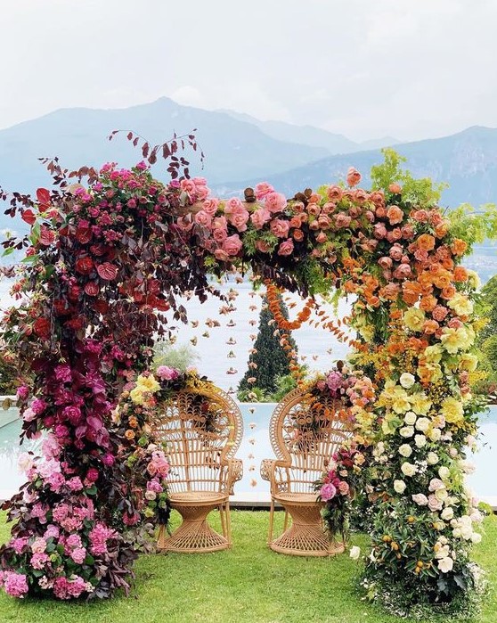 a bold lush floral wedding arch from light pink to mauve, burgundy, peachy pink, orange and yellow florals is a statement idea