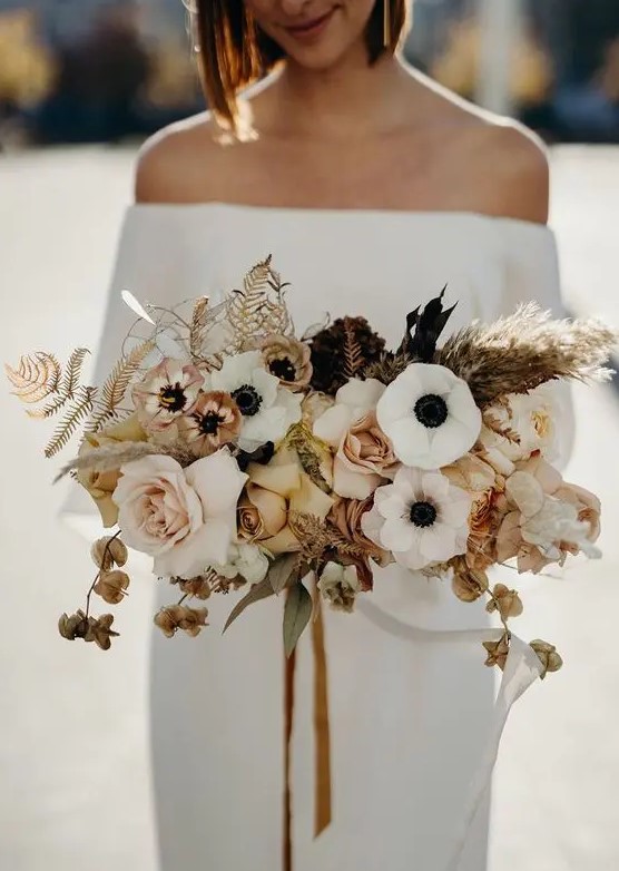 a stylish modern wedding bouquet of white anemones, blush and rust roses, dried blooms, leaves and grasses and mustard ribbons