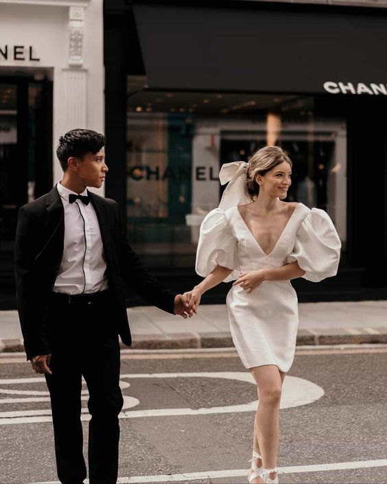 an over the knee plain wedding dress with a plunging neckline and puff sleeves, lace up shoes and a bow in the hair is trendy and cool