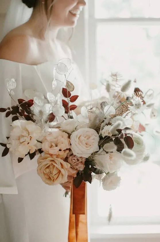 a soft pastel wedding bouquet with white and blush blooms plus herbs and orange ribbons for a delicate look