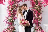 11 a bold wedding ceremony space with an arch covered with greenery, blush, hot pink and fuchsia blooms and planters with matching blooms