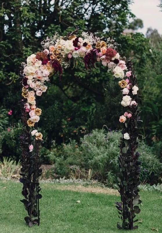 a beautiful moody Halloween wedding arch decorated with dark foliage, with neutral, pastel and dark blooms