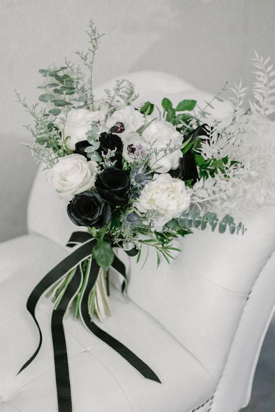 a black and white wedding bouquet of roses, greenery, thistles and white leaves plus black ribbons is amazing