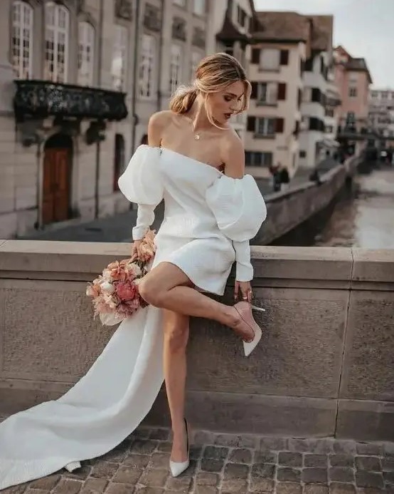 a sexy 90s inspired mini wedding dress with puff sleeves and a long train, nude shoes and a necklace for a super hot look