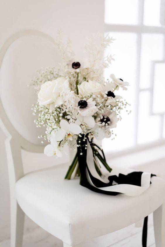 a chic black and white wedding bouquet of white orchids, roses and anemones, baby's breath, some black and white ribbons