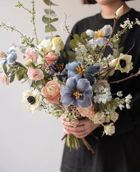 a beautiful and delicate pastel wedding bouquet of peachy ranunculus, blue and white blooms, eucalyptus and blooming branches