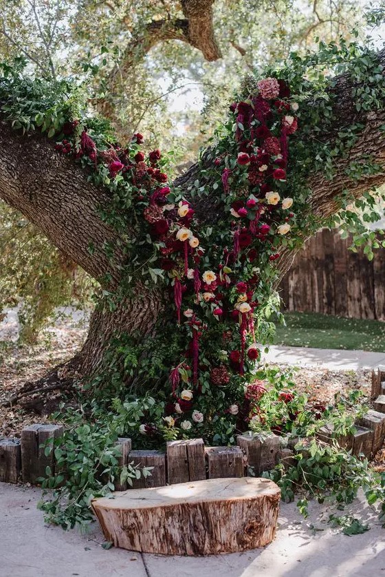 a living tree wedding altar with greenery, peachy and burgundy blooms, lisianthus and amaranthus is a gorgeous idea for a jewel tone wedding