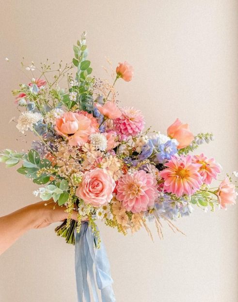 a beautiful pastel summer wedding bouquet of pink roses and dahlias, blue and white blooms and greenery is amazing for the season