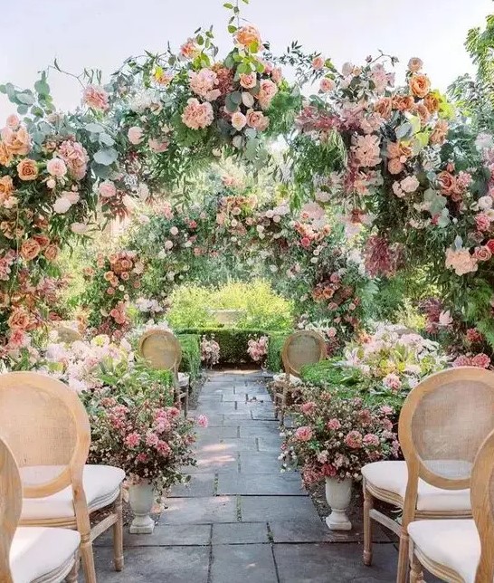 a pastel flower garden wedding ceremony space with greenery and pink bloom arches and floral arrangements on the ground