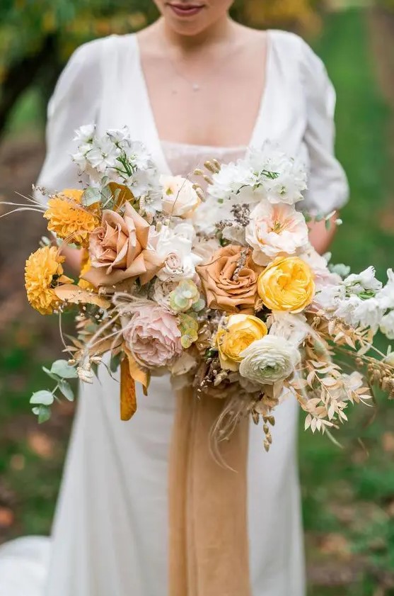 a delicate and pretty fall wedding bouquet of yellow, blush, rust blooms, greenery and dried foliage for a subtle fall bridal look