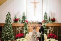 a Christmas wedding ceremony space with golden and red poinsettias and lots of Christmas trees with lights is wow